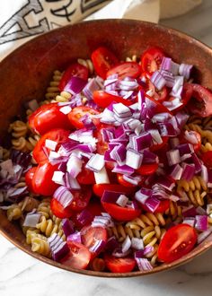 pasta salad with tomatoes, onions and red onion in a copper bowl on a marble countertop