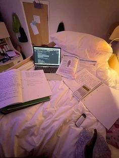 an open laptop computer sitting on top of a bed next to books and other items