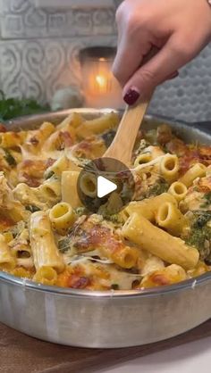 a person stirring pasta in a pan with a wooden spoon on a counter top next to a lit candle