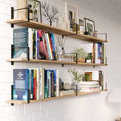 two wooden shelves with books on them against a white brick wall