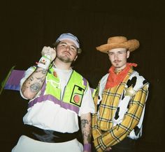 two men dressed in costumes standing next to each other with one holding a beer bottle