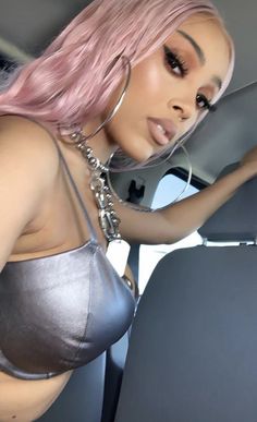 a woman with pink hair wearing a silver bra and chain around her neck, in the back seat of a car