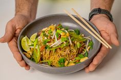 a person holding a bowl of food with chopsticks