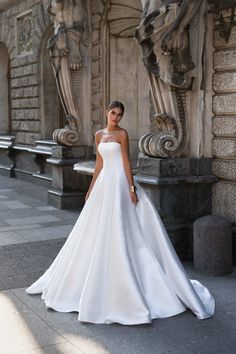 a woman in a white wedding dress standing on the sidewalk near an ornate stone building