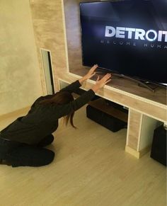 a woman kneeling on the floor in front of a large television screen that reads detroit become human