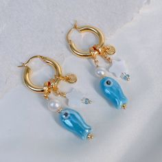 Immerse yourself in the whispers of the sea with these enchanting earrings. Inspired by the dance of ocean waves, delicate ceramic fish, lustrous pearls, and gleaming seashells unite to create a symphony of romance. Let the golden hoops embrace you in the warmth of a sunlit coastal breeze, embodying the magic of a seaside love story. Composition: pearl/shell/glass/ceramic/925 silver/gold-plated brass Avoid exposure to harsh chemicals, such as perfume, hairspray, and cleaning agents. Store your m Story Composition, Sea Earrings, Ocean Earrings, Coastal Breeze, The Whispers, Golden Hoops, White Pearl Earring, Ceramic Fish, Slow Fashion Brands