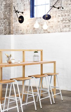 three stools and a table in front of a brick wall with lights hanging from it