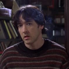 the young man is sitting in front of bookshelves and looking off to his left