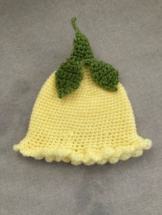 a crocheted yellow beanie with green leaves on the top, sitting on a gray surface