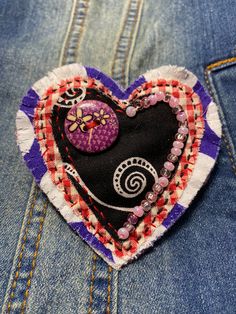 a close up of a heart shaped brooch on a pair of blue jeans with buttons