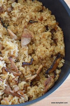 a pan filled with rice and meat on top of a wooden table