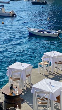 tables and chairs are set up on the dock by the water with boats in the background