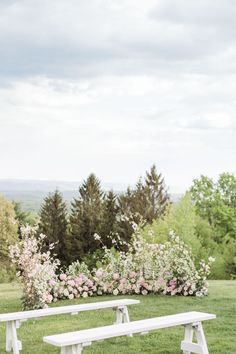 two white benches sitting on top of a lush green field next to trees and flowers