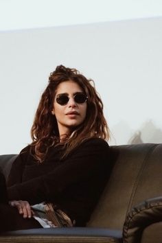 a woman sitting on top of a brown couch wearing sunglasses and looking off to the side