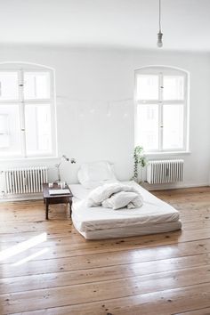 an unmade bed sitting on top of a wooden floor next to two large windows