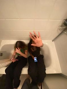 two people sitting in a bathtub with their hands up to the ceiling and one person standing next to them