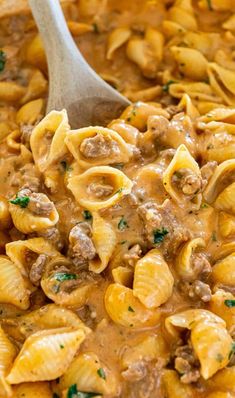 a wooden spoon in a pot filled with pasta and meat sauce on top of it