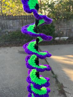 a purple and green crocheted wind chime hanging from a wire on the sidewalk