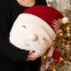 a woman holding a stuffed santa clause in front of a christmas tree