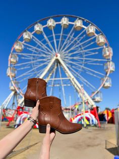 someone is holding up their brown boots in front of a ferris wheel and blue sky