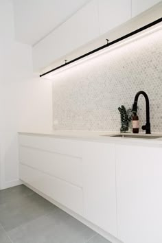 a white kitchen with black faucet, sink and tile backsplashing