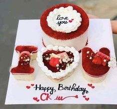 a person holding up a birthday card with two cakes in the shape of heart and booties