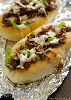 two sandwiches with meat, cheese and peppers on tin foil