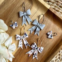 four bows are hanging from earrings on a tray next to flowers and wicker basket