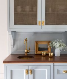 a kitchen with white cabinets and gold hardware on the countertop, along with a vase filled with baby's breath flowers