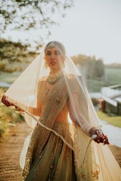 a woman in a green and gold wedding dress holding a white veil over her head