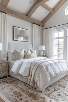 a large white bed sitting in a bedroom next to a window with curtains on it