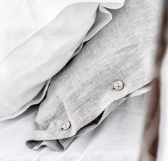 an unmade bed with white linens and buttons on the pillowcase, in black and white