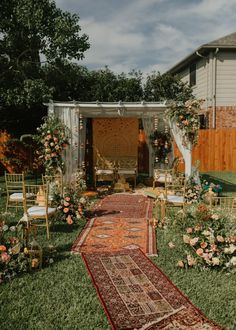 an outdoor ceremony setup with chairs and rugs in the grass, surrounded by flowers