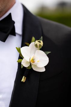 a man wearing a black tuxedo with white flowers on it's lapel