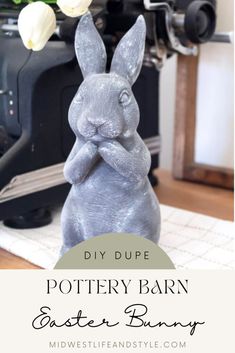 a gray bunny statue sitting on top of a table next to a camera and flowers