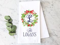 a white towel with the letter l on it next to some leaves and a plant