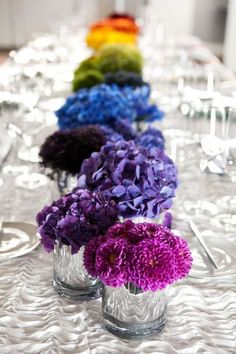 several vases filled with purple and green flowers on a white tablecloth covered table