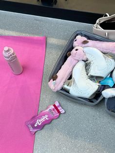 an open suitcase filled with shoes and other items next to a pink mat on the ground