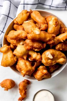 a white bowl filled with fried food next to a cup of ranch dressing on top of a table