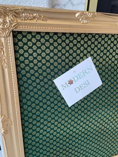 an ornate gold frame holds a sign that reads modern desi on it and sits against a marble wall