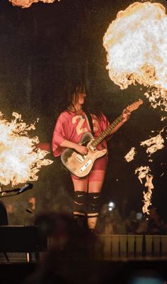 a woman playing guitar in front of fire and flames on the stage at a concert