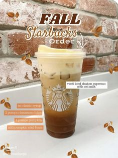 a starbucks drink sitting on top of a white counter next to a brick wall with leaves