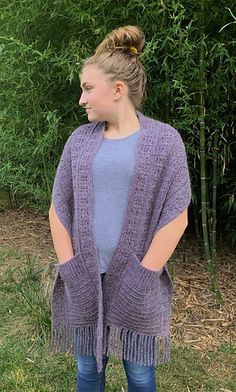 a woman standing in the grass wearing a purple knitted shawl with fringes