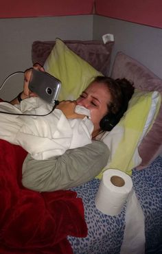 a woman laying in bed with her headphones on and holding a cell phone to her ear