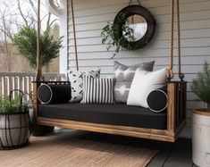 a porch swing with pillows and plants on it