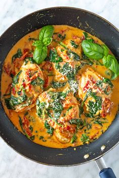 a skillet filled with chicken and spinach covered in sauce on top of a white counter