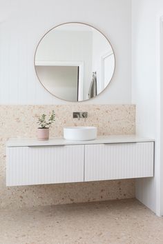 a white bathroom vanity with a round mirror above it