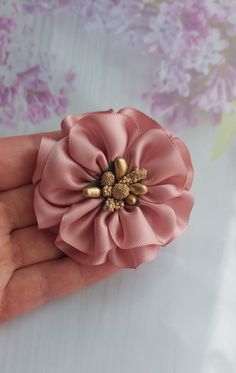 a hand holding a pink flower with gold accents