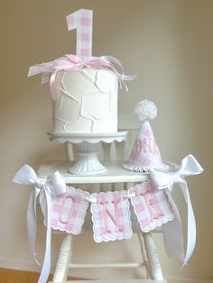 a pink and white first birthday cake on a wooden stand with decorations for it's first birthday