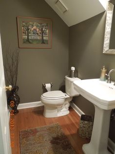 a white toilet sitting next to a sink in a bathroom under a painting on the wall